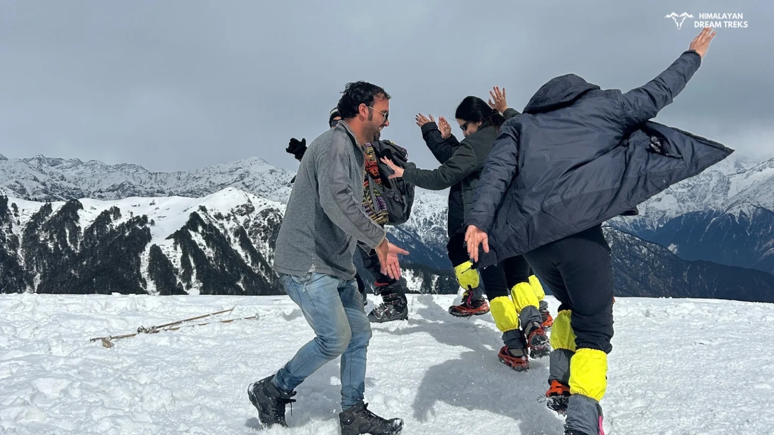 A group of trekkers dancing and enjoying at Dayara Bugyal with the majestic Himalayas in the background.