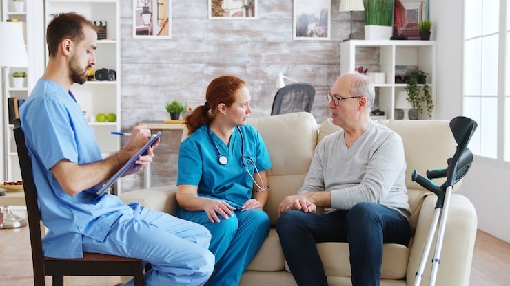 team of male and female nurses talking with an old and retired man in bright and cozy nursing home