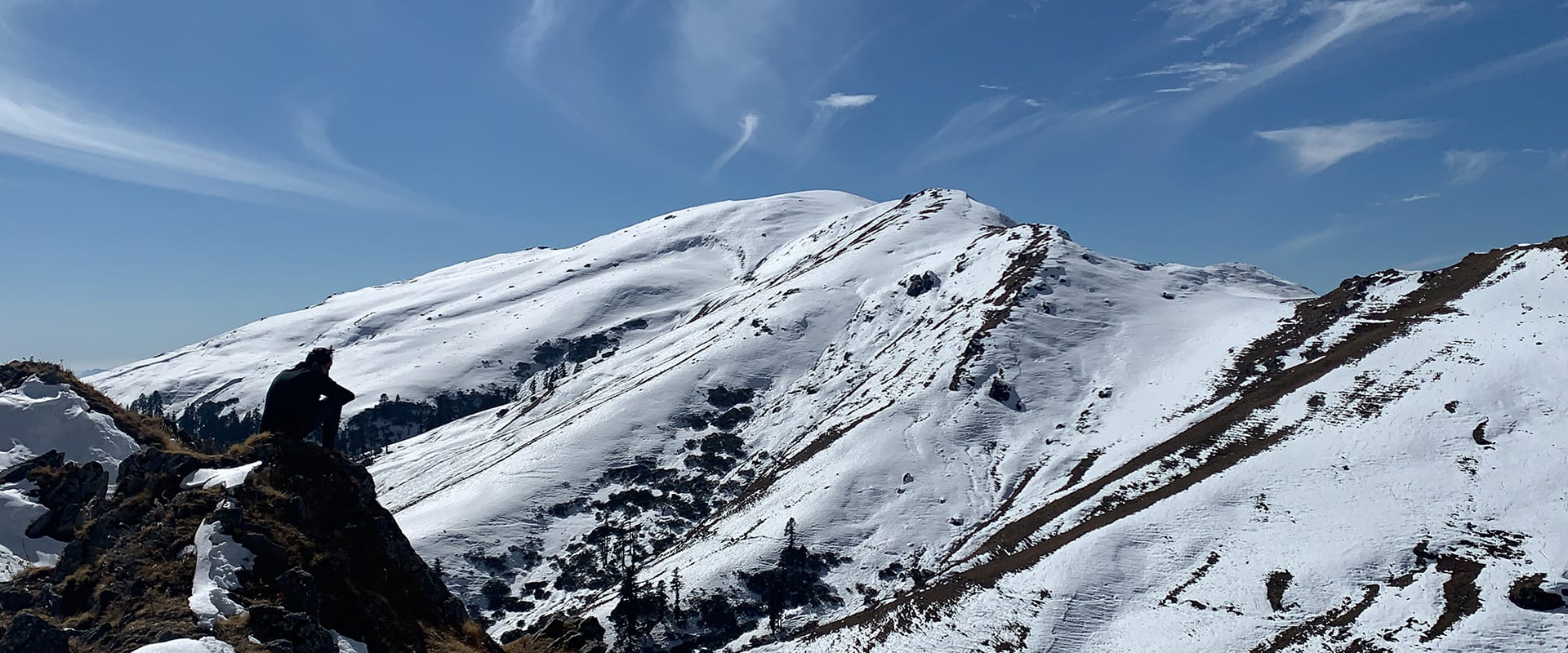 A trekker standing in awe of the endless snow expanse of Dayara Bugyal.